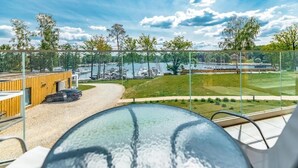 A modern outdoor seating area with a glass table and chairs, overlooking a marina with boats and a grassy landscape. - Stranda Residence Apartments Giżycko (Giżycko)