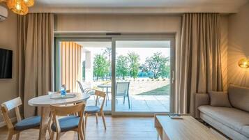 A hotel room with a dining area, a sofa, and a sliding glass door leading to an outdoor area with trees.
