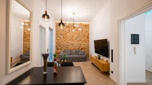 Ein modernes Wohnzimmer mit Steinwand, einem grauen Sofa, einem Fernseher und einem Essbereich mit Tisch und Stühlen.