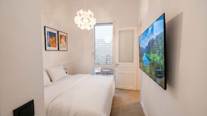 Ein Schlafzimmer mit Bett, einem an der Wand befestigten Fernseher und einem Fenster mit Blick auf einen Balkon.