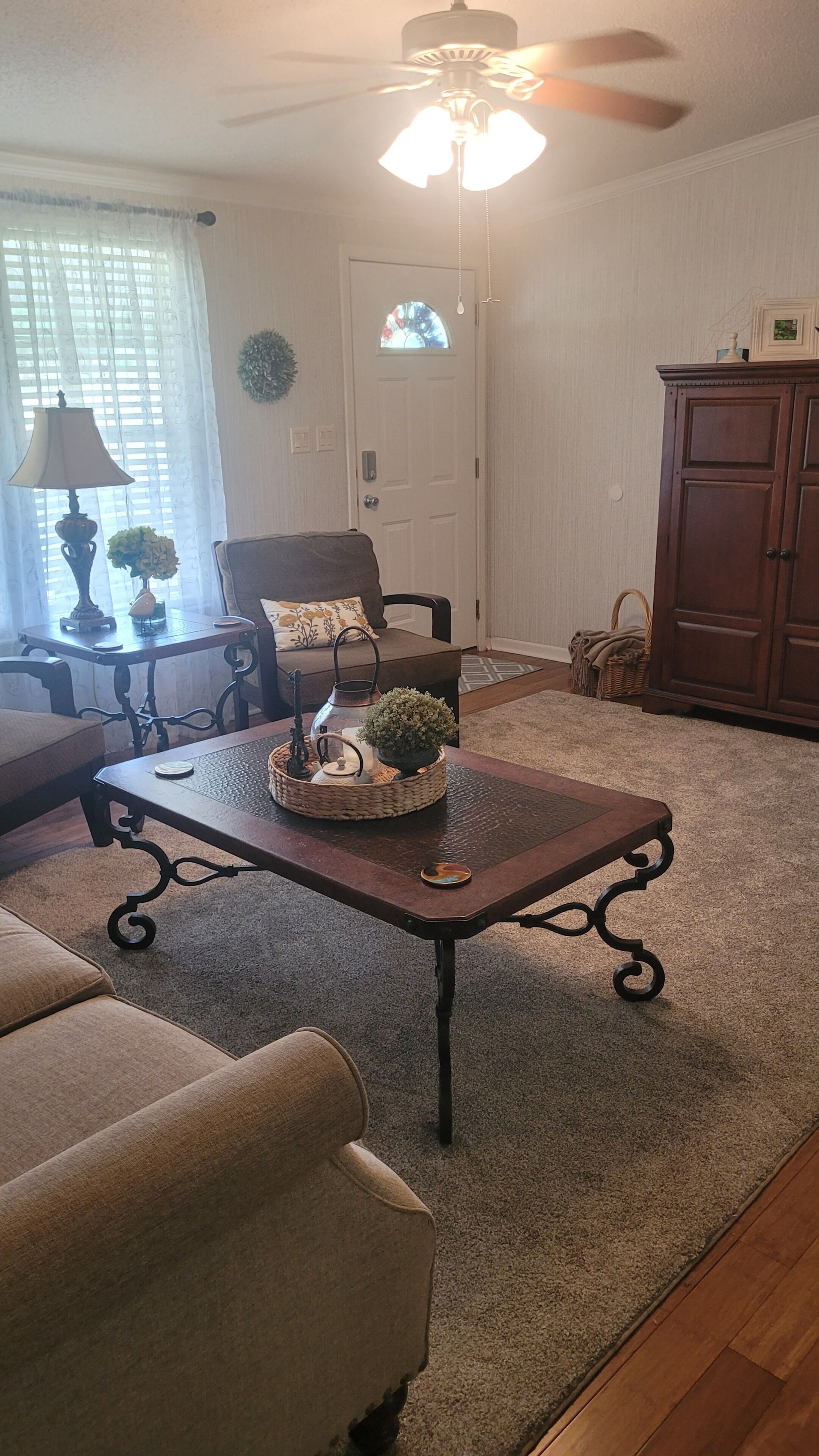 A living room with a ceiling fan, a coffee table with decorative items, a sofa, and a door with a window.