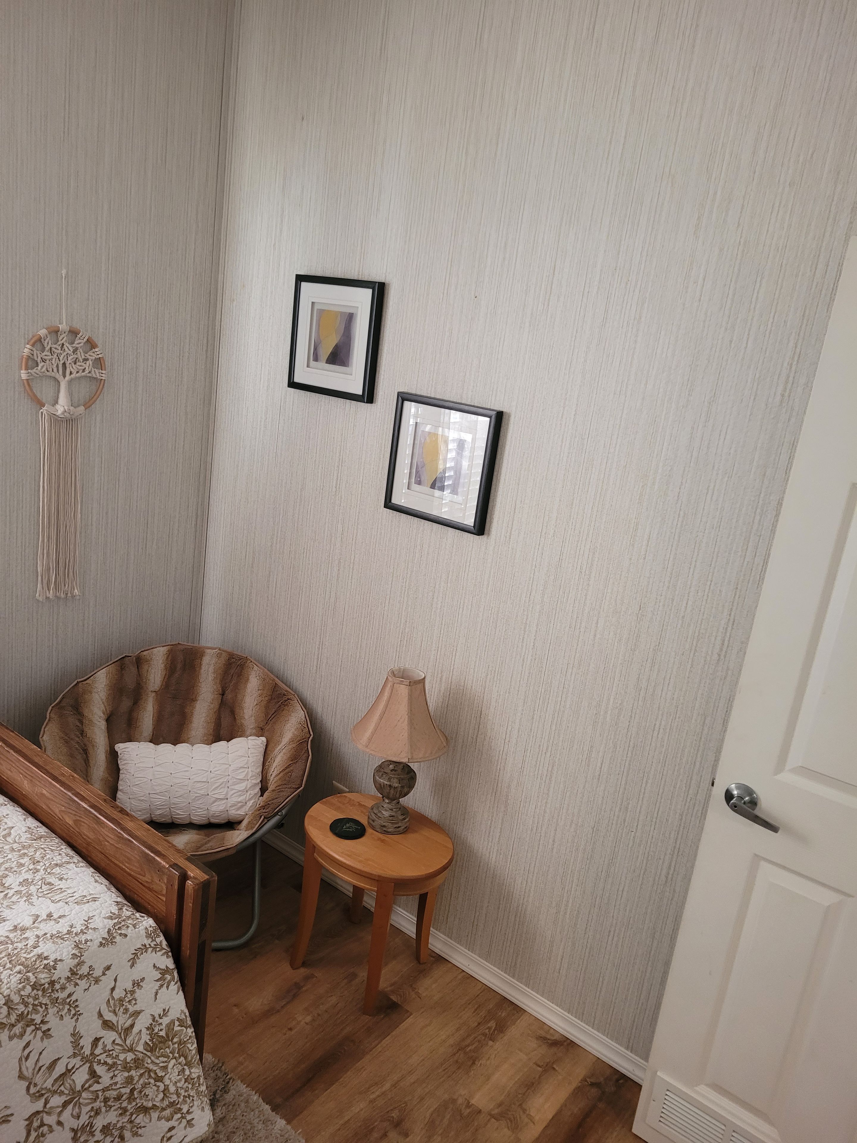 Ein Zimmer mit einem Bett, einem Sessel, einem kleinen Tisch mit einer Lampe und zwei gerahmten Bildern an der Wand.