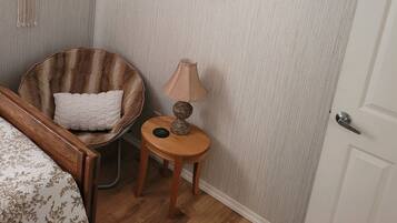 Ein Zimmer mit einem Bett, einem Sessel, einem kleinen Tisch mit einer Lampe und zwei gerahmten Bildern an der Wand.