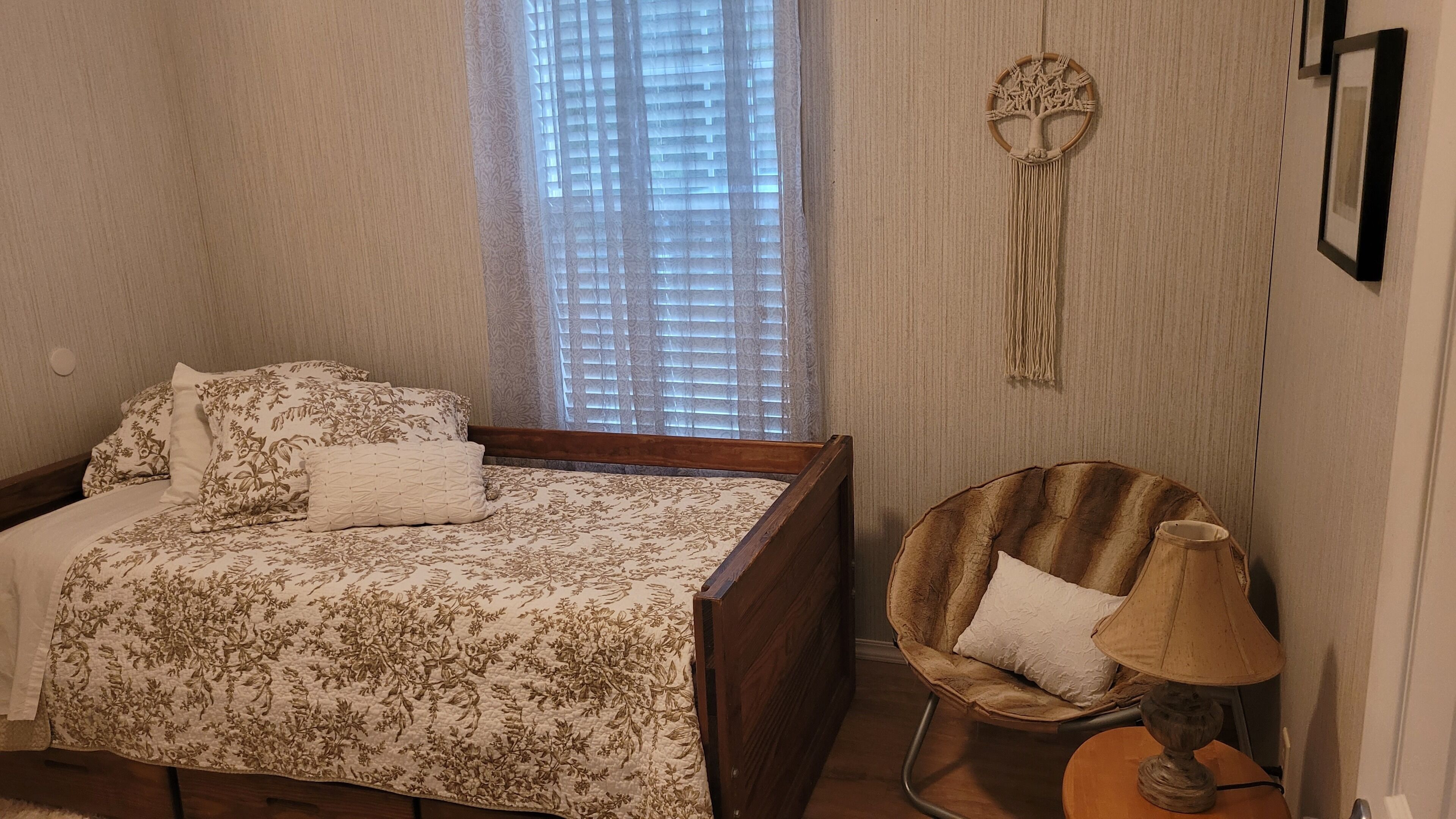 A bedroom with a bed, a chair, a lamp, and a wall decoration.