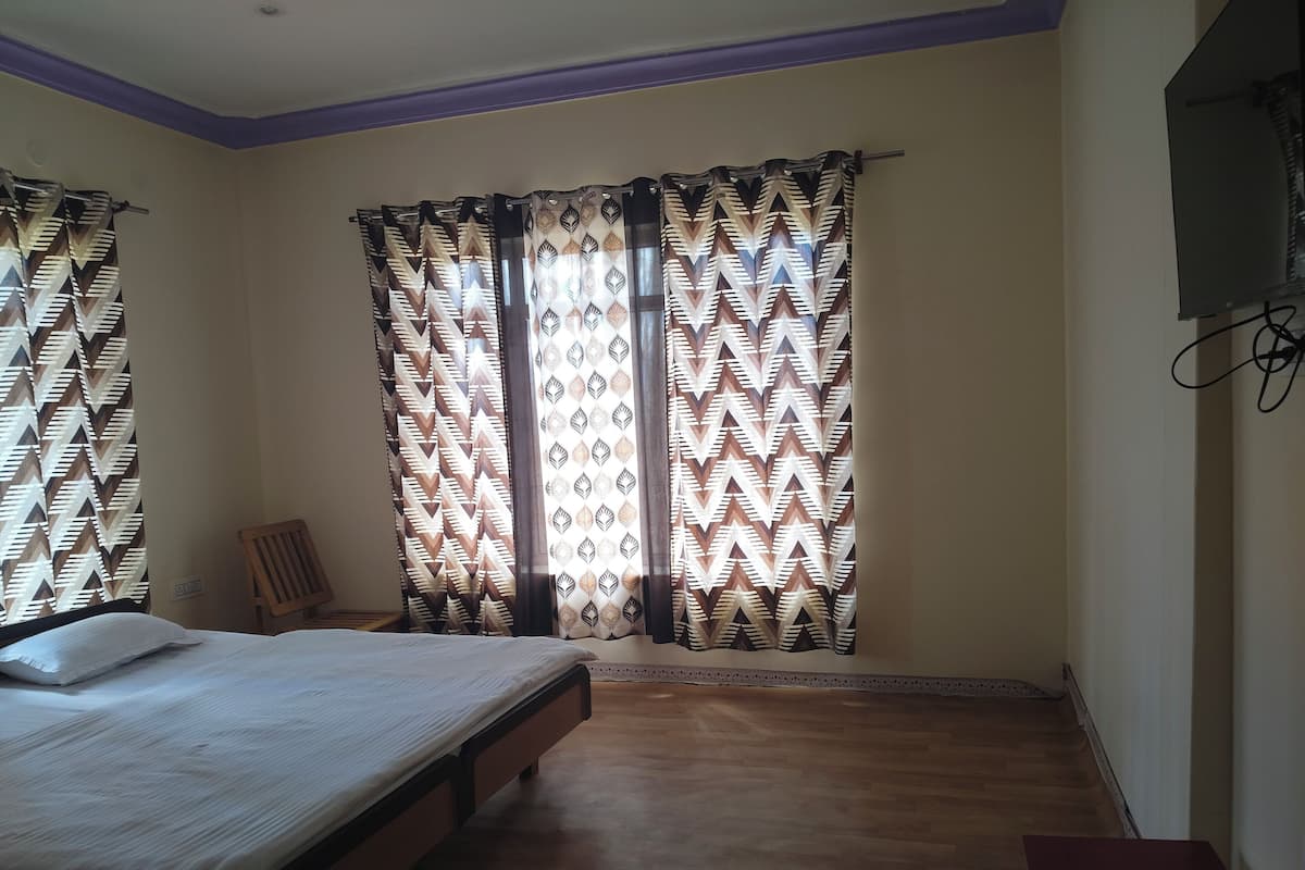 A bedroom with a bed, a wooden chair, and patterned curtains.