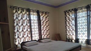 A bedroom with a bed, curtains, a chair, and a wooden floor. - Donskit guest house  (Leh)