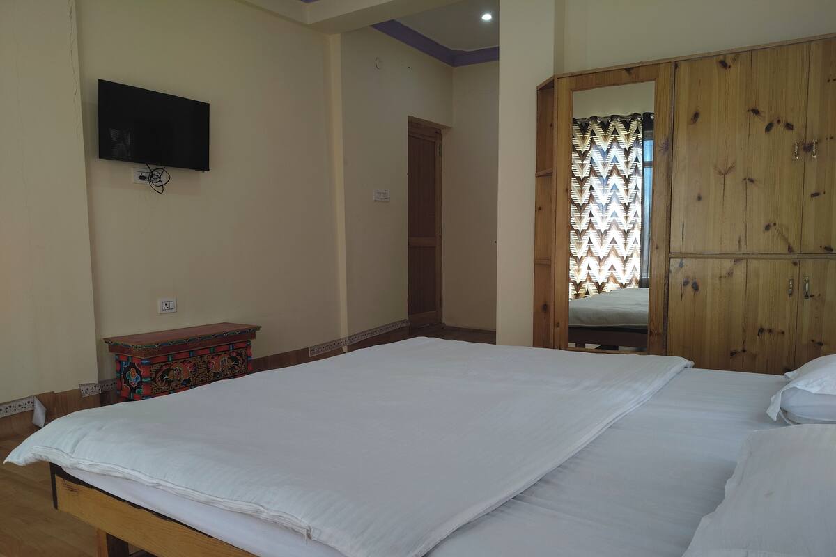 A bedroom with a large bed, a television mounted on the wall, and a wooden wardrobe.
