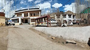 A building with a large entrance, a small porch, and a vehicle parked in front. - Donskit guest house  (Leh)