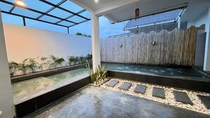 Un espace piscine extérieur moderne doté d’un toit en verre, d’une clôture en bois et d’un chemin pavé de galets.