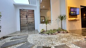 Une entrée moderne avec un portail en bois, un petit jardin agrémenté de plantes et un téléviseur fixé au mur.