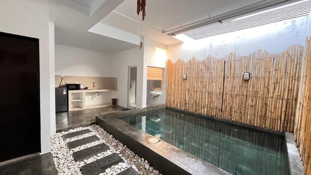 Un intérieur moderne avec une piscine à fond de verre, un mur en bambou et un espace cuisine.