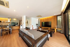 A modern living room with a sofa, TV, wooden flooring, and a dining area.