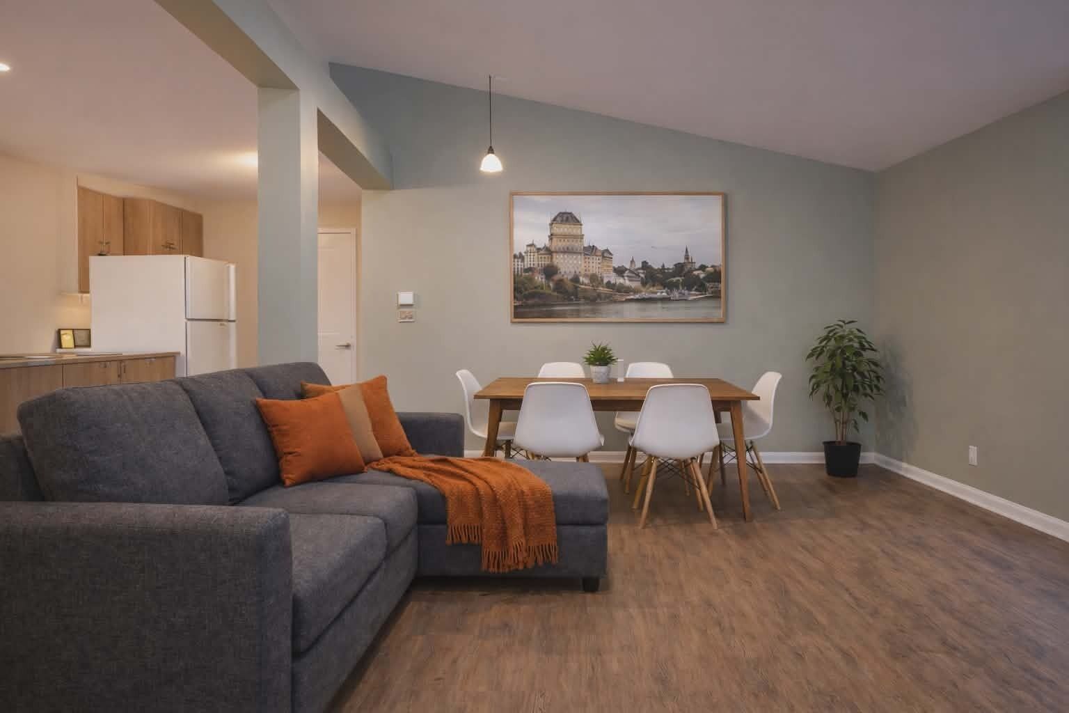 Un salon avec un canapé, une table à manger entourée de chaises, un coin cuisine et un tableau encadré au mur.