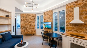 Eine moderne Küche mit Steinwänden, eine Essecke mit Tisch und Stühlen, ein Sofa und ein an der Wand befestigter Fernseher.