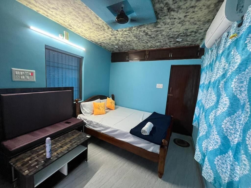 Una habitación con cama, un banco, una ventana con persianas, un ventilador de techo y un equipo de aire acondicionado.