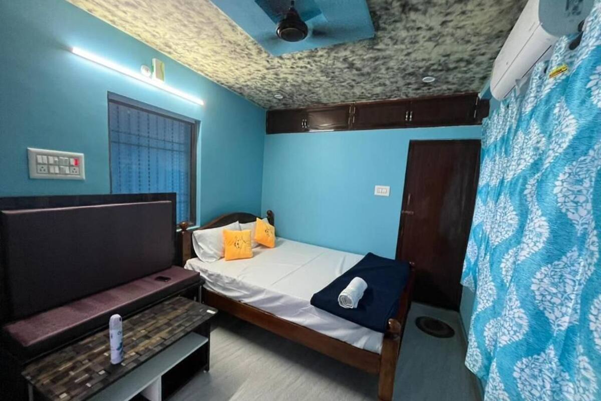 A room with a bed, a bench, a window with blinds, a ceiling fan, and an air conditioning unit.