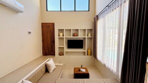 A living room with a sofa, a coffee table, a TV on a shelf, and a door.