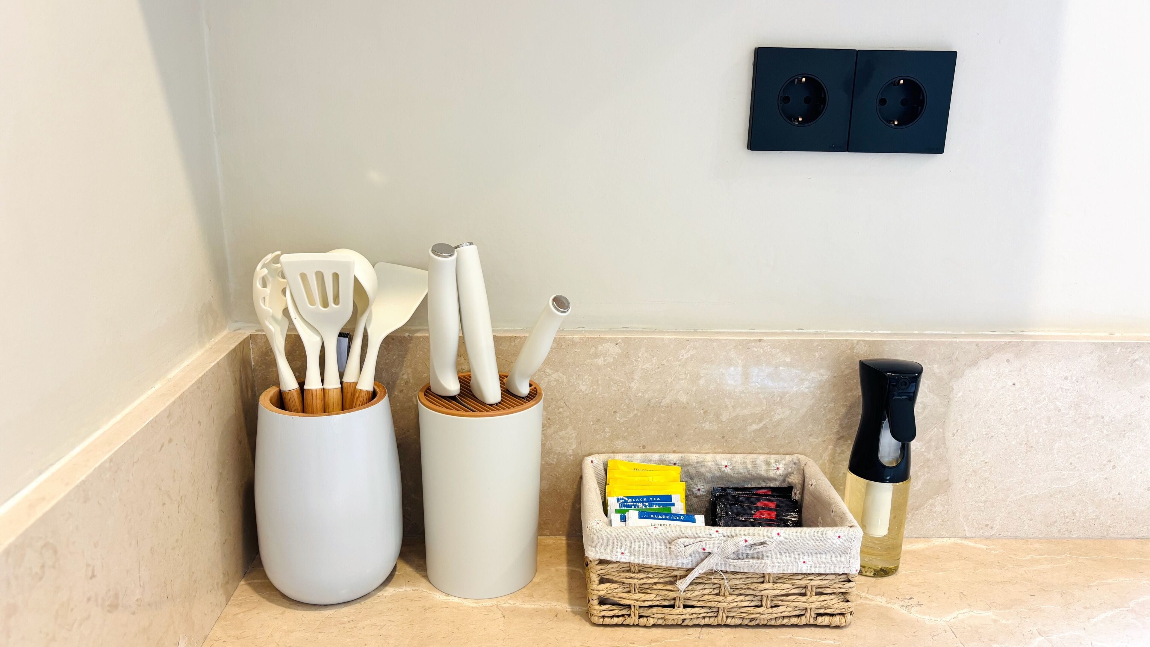 A kitchen counter with utensils, a basket of tea bags, and a water bottle.