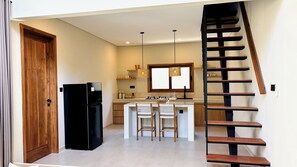 Eine Küche mit einer zentralen Kochinsel, Holzstühlen, einem schwarzen Kühlschrank und einer Holztreppe.