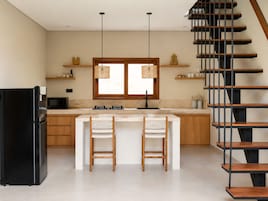 Una cocina moderna con una isla central, sillas de madera, un refrigerador negro, un microondas y una escalera.