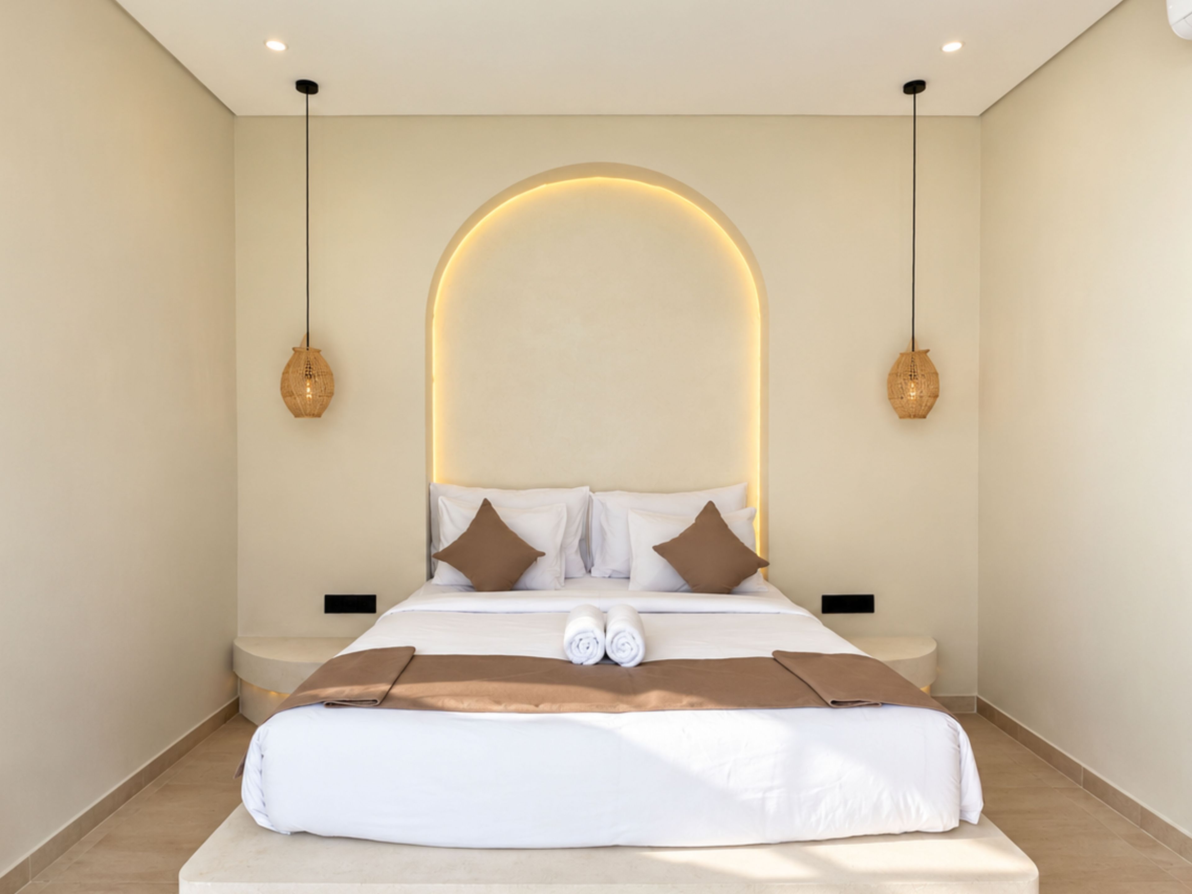 A modern hotel room with a large bed, two bedside tables, and a unique arched ceiling light fixture.