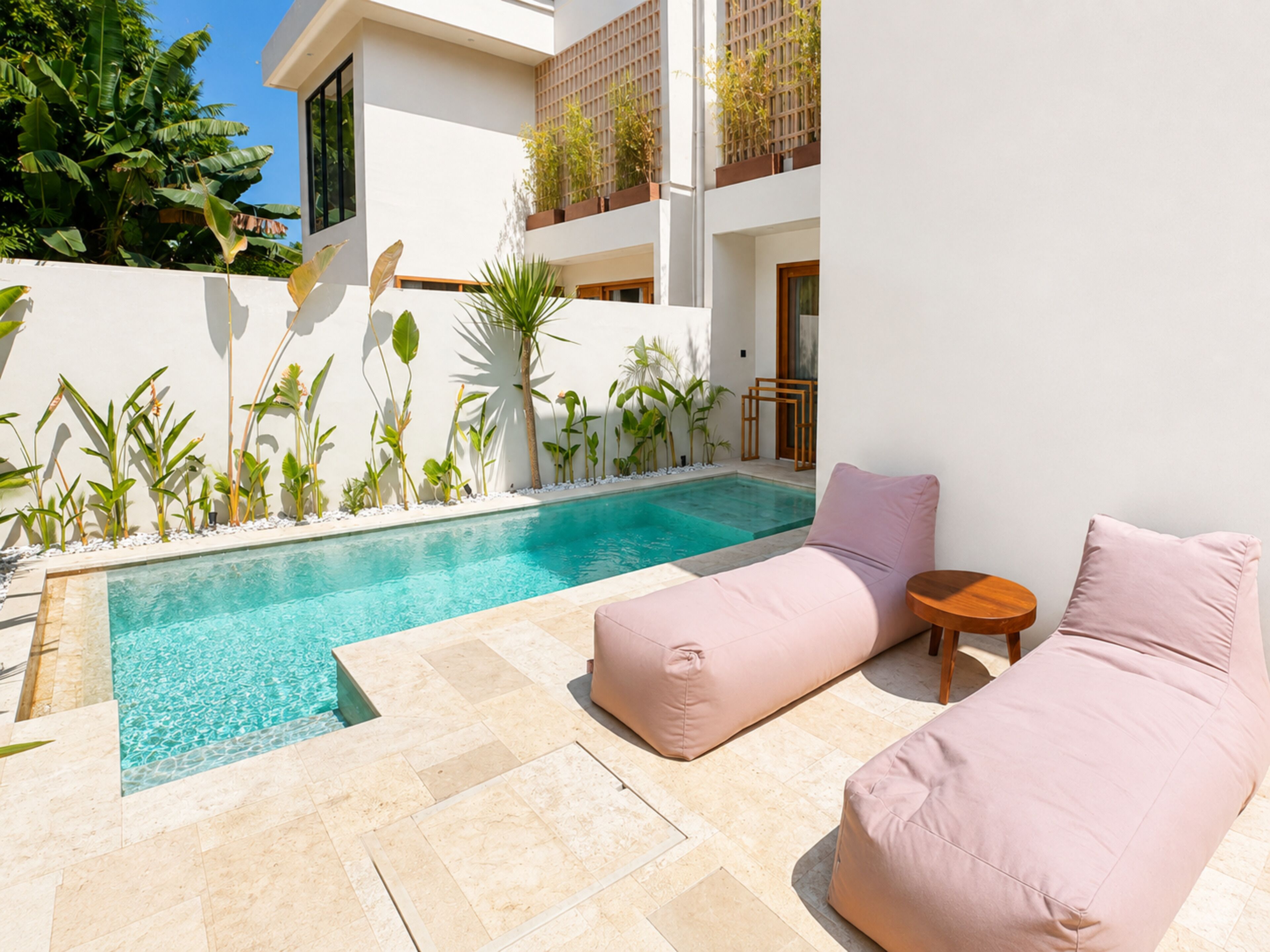 A pool area with a chaise lounge and a small table, surrounded by tropical plants.