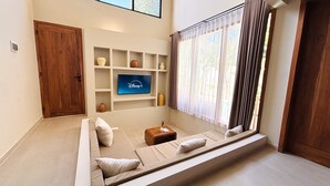 A living room with a sofa, a TV mounted on the wall, and a window with curtains.