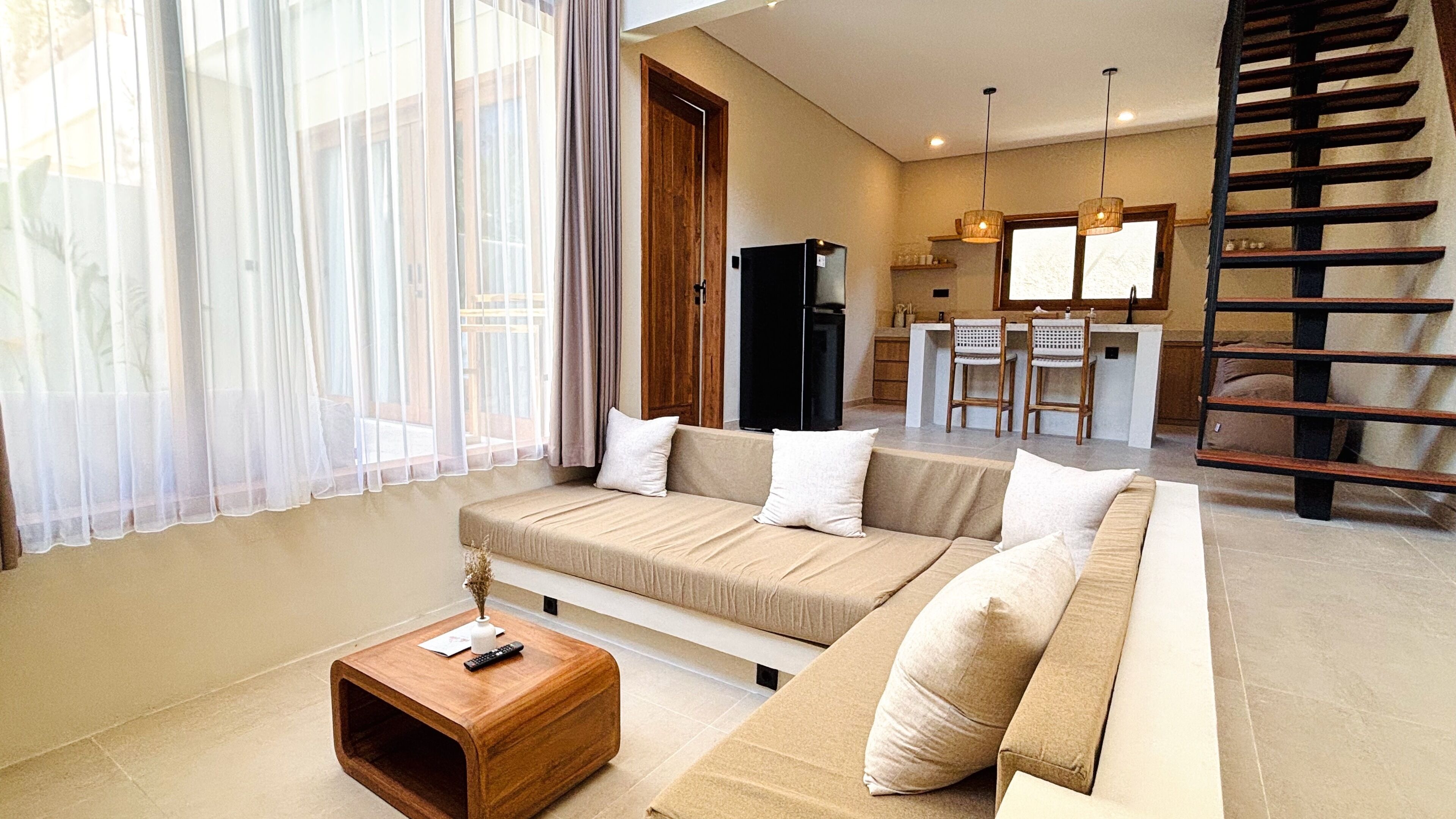 A living room with a sofa, a coffee table, and a kitchen area with a refrigerator and bar stools.