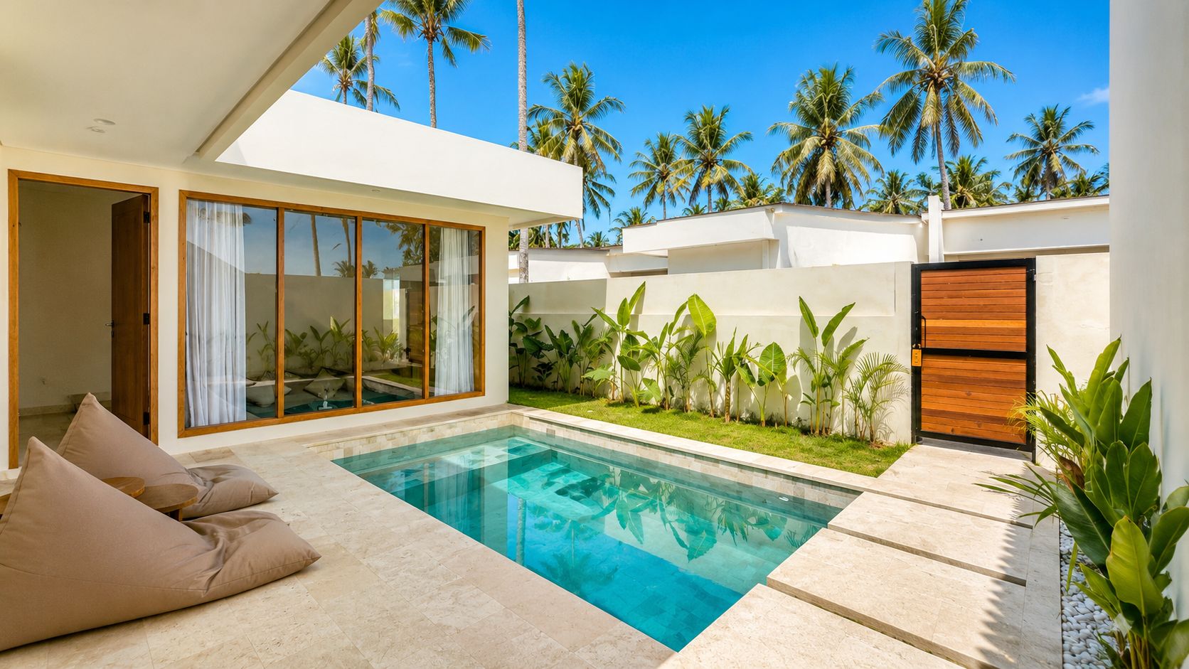 Ein moderner Poolbereich mit einem klaren, blauen Pool, einer Lounge-Ecke mit Sitzkissen und Blick auf Palmen.