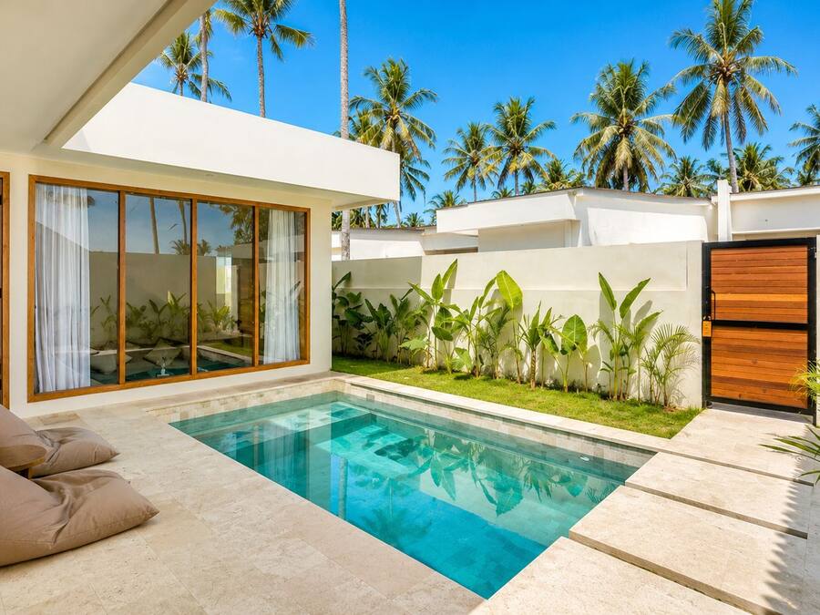 A modern pool area with a clear blue pool, a seating area with cushions, and a view of palm trees.