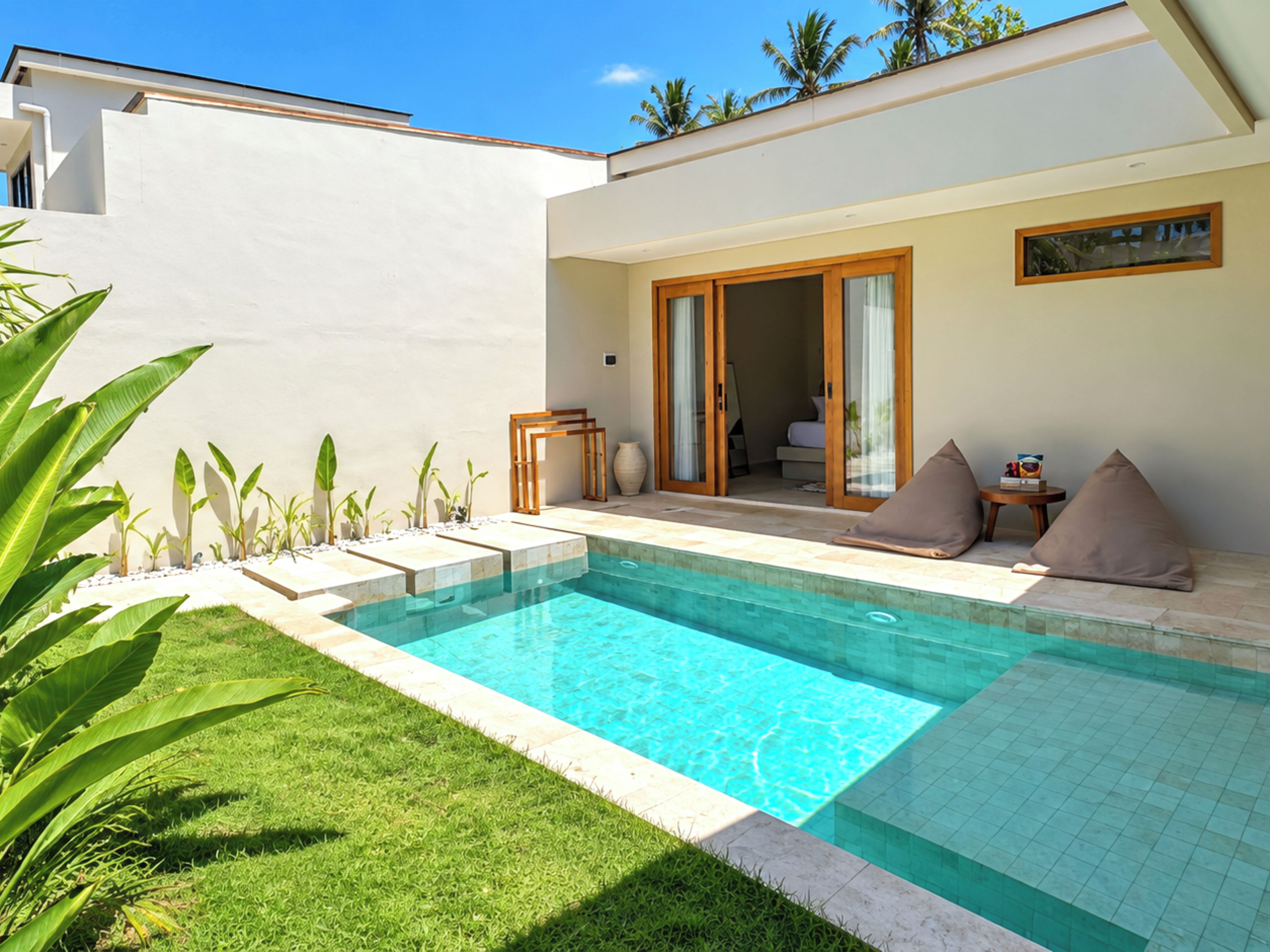 A modern outdoor swimming pool with a clear blue water, surrounded by a well-maintained lawn and tropical plants.