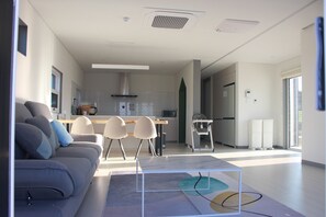 Uma sala de estar moderna com um sofá, cadeiras, uma mesa de centro e uma cozinha com uma mesa de jantar e cadeiras.