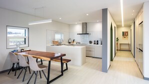 A modern kitchen with a central island, a dining area with a wooden table and chairs, and a view of a cityscape through a window.