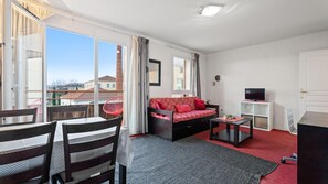 Une pièce comprenant un canapé, une table à manger avec des chaises, un téléviseur et une fenêtre avec des rideaux.