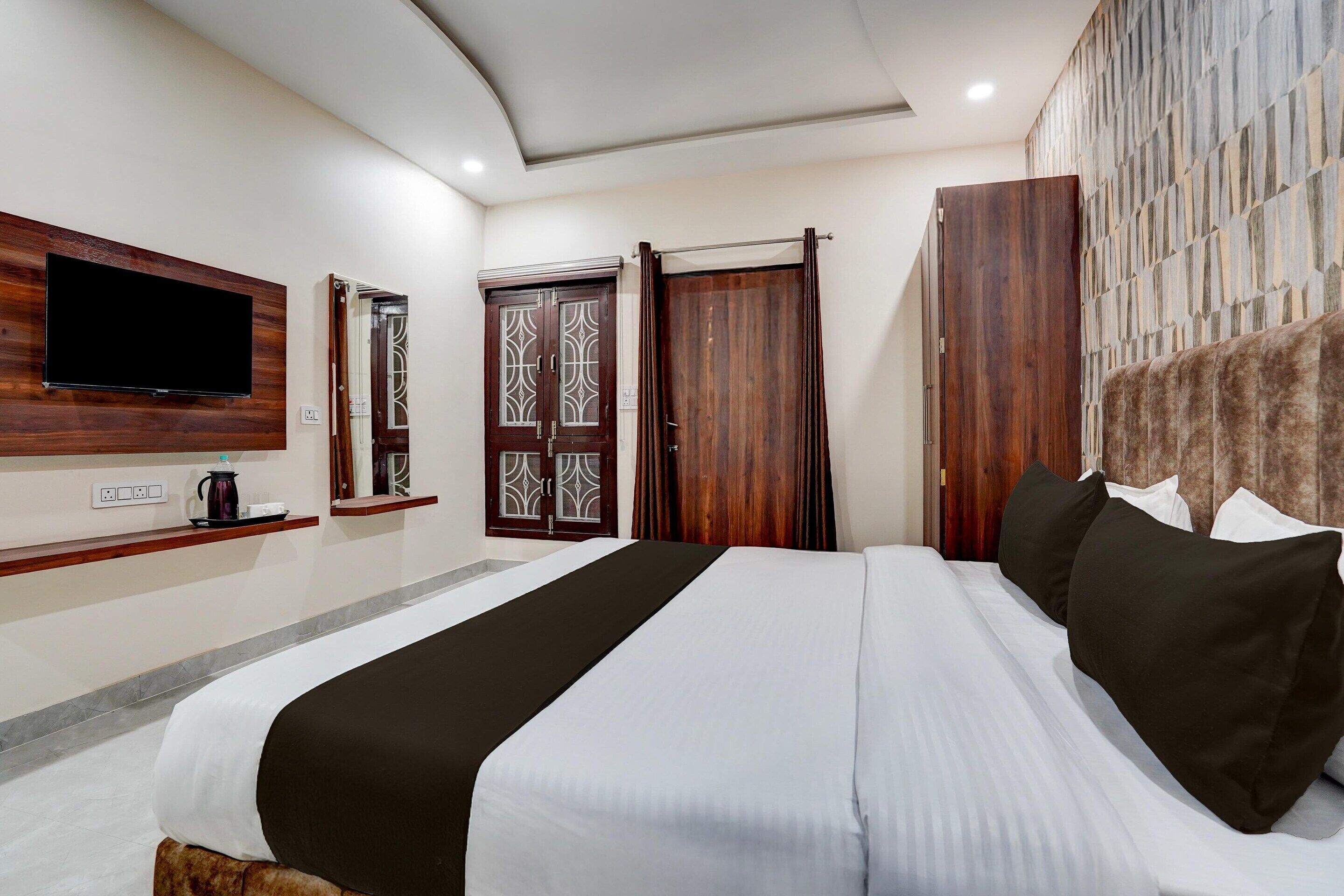 A hotel room with a bed, a flat-screen TV mounted on the wall, a wooden wardrobe, and a stone-patterned wall.