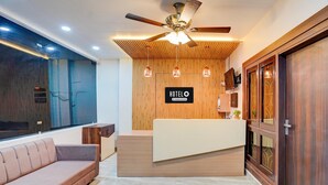 A hotel reception area with a wooden reception desk, a sofa, a ceiling fan, and a sign that reads 'HOTEL O Company Services'. - Premium Neelam Hotel (Bareilly)