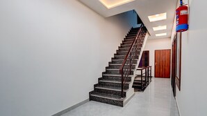 A staircase with a handrail, a fire extinguisher on the wall, and a wooden door at the bottom. - Premium Neelam Hotel (Bareilly)