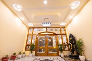 Entrada de hotel con una puerta de madera imponente, un candelabro y plantas en macetas.