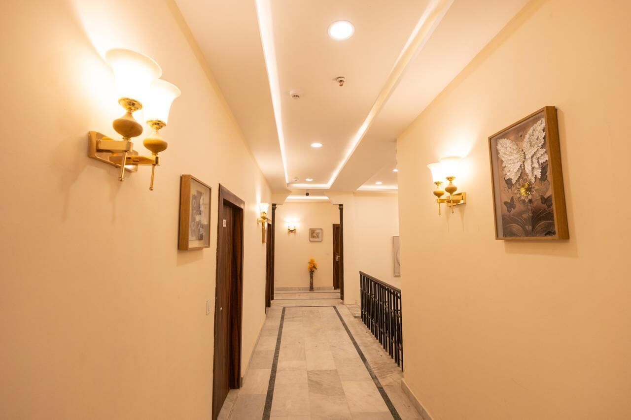Un couloir d’hôtel avec des luminaires fixés au mur, des œuvres d’art encadrées et un sol en marbre.