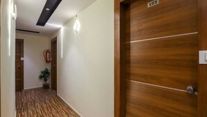 Ένας διάδρομος με ξύλινο δάπεδο, μια πόρτα με την ένδειξη «105», ένας πυροσβεστήρας και μια γλάστρα με φυτό.