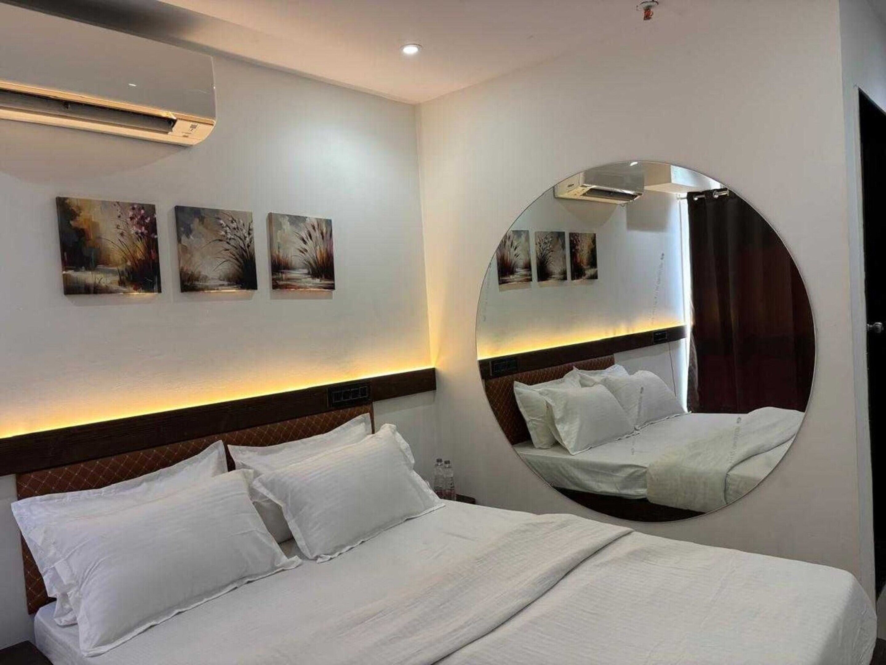 A hotel room with a bed, a round mirror, and three wall-mounted paintings.
