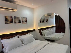A hotel room with a bed, a round mirror, and three wall-mounted paintings. - Deluxehotel Daman (Daman)