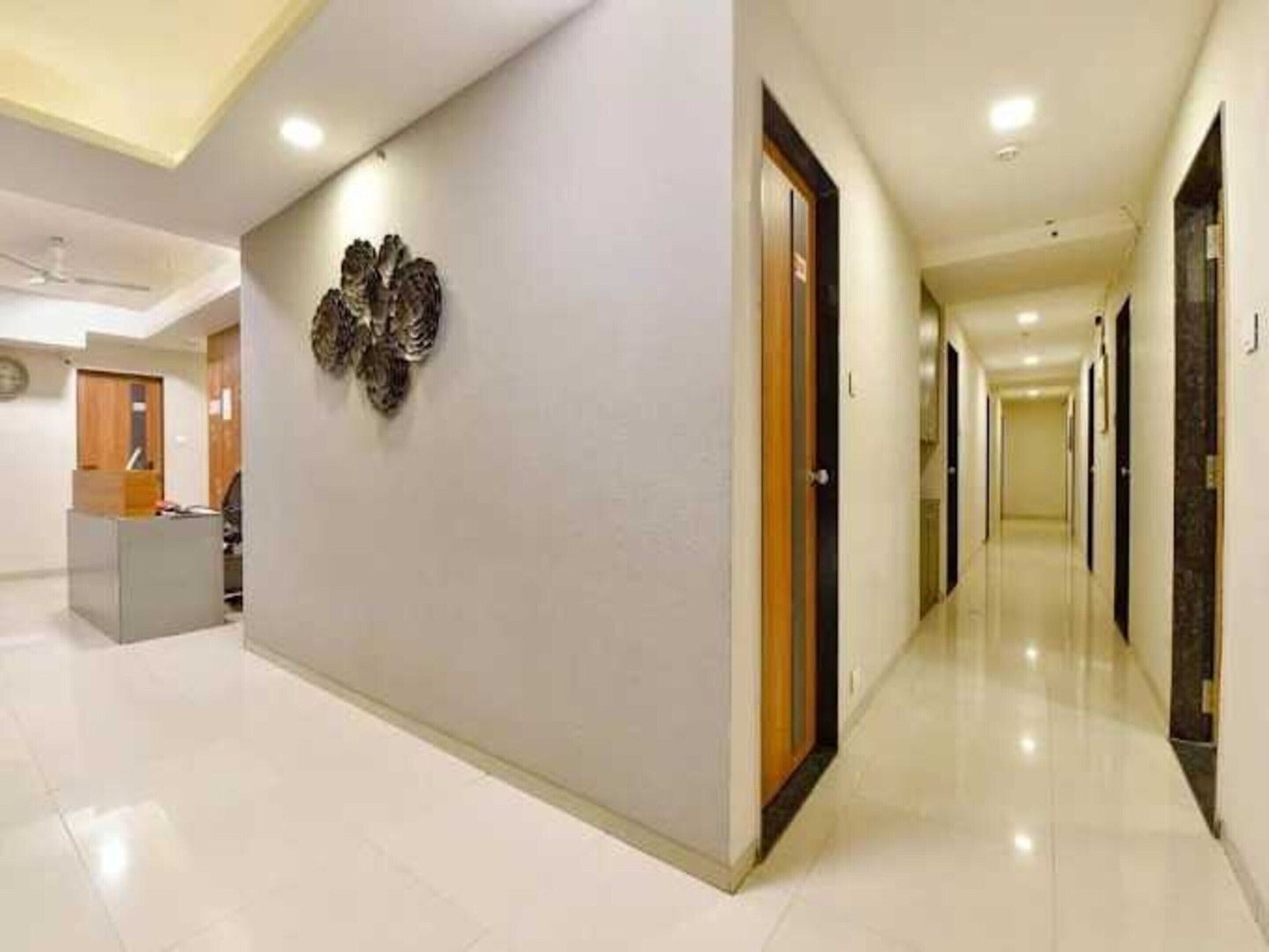 A hotel corridor with a reception desk, a decorative wall piece, and doors leading to rooms.