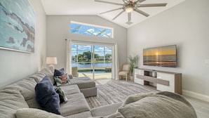 A living room with a sofa, TV, ceiling fan, and a view of a lake through glass doors. - Huge Pool, Near Beaches, IMG, UTC, Great Clubhouse (Bradenton)