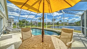 A poolside area with a table and chairs, a yellow umbrella, and a view of a lake and houses. - Huge Pool, Near Beaches, IMG, UTC, Great Clubhouse (Bradenton)