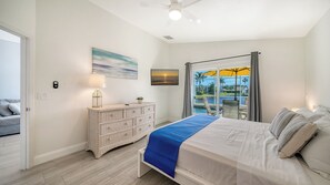 A bedroom with a bed, a dresser, a television, and a view of a pool and palm trees. - Huge Pool, Near Beaches, IMG, UTC, Great Clubhouse (Bradenton)