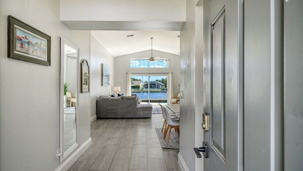 A hallway with a grey sofa, a dining table, and a view of a body of water through large windows. - Huge Pool, Near Beaches, IMG, UTC, Great Clubhouse (Bradenton)