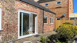 A brick house with a sliding glass door, a small garden, and a wooden fence. - Lamp Post Cottage 3 - UK50955 (Bridlington)