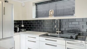 A modern kitchen with white cabinets, a black tiled backsplash, a stainless steel sink, and a built-in oven. - Lamp Post Cottage 3 - UK50955 (Bridlington)