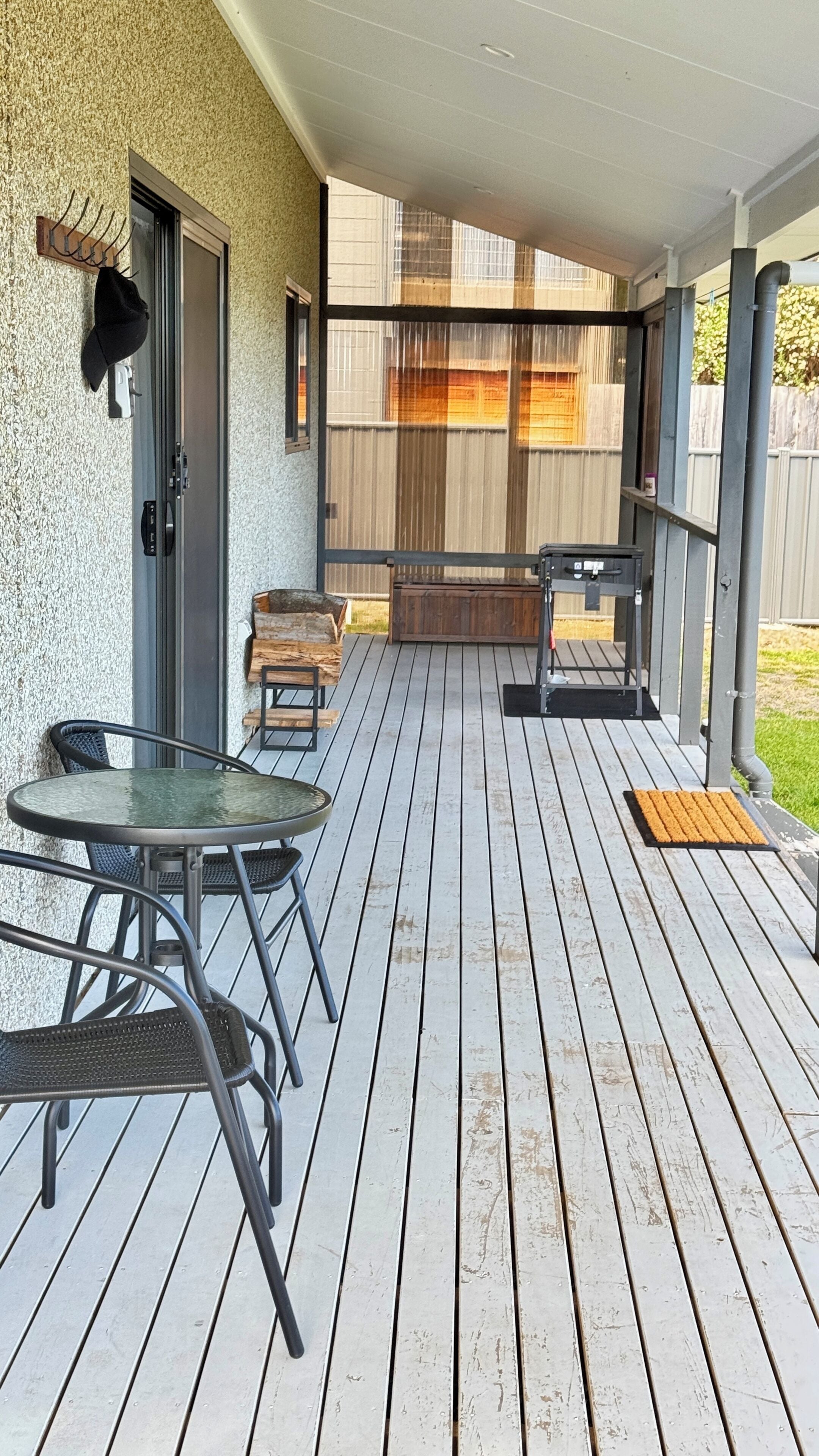 A covered outdoor patio with a table and chairs, a door, and a window with blinds.